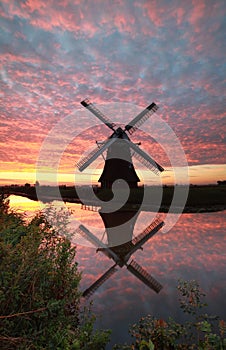 Windmill and dramatic sunrise sky reflected in river