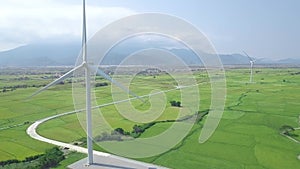 Windmill energy plant power turbine in agricultural field. Aerial view wind power generation on green field and mountain