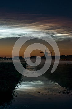 Noctilucent clouds over a classic dutch landscape at night with windmill along a canal.