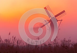 Windmill in foggy colorful sunrise.