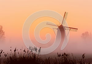 Windmill in foggy colorful sunrise in the countryside.