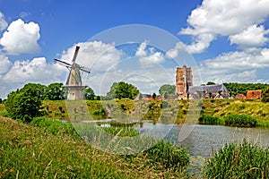 A windmill on the fortifications and a church behind the fortifications of the town of Woudrichem surrounded by the waters of two