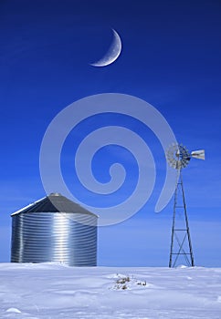 Windmill and Grain Silos in Winter Snow on Farm for Agricultural Farming with Crescent Moon