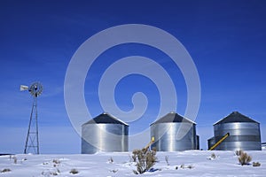 Windmill and Grain Silos in Winter Snow on Farm for Agricultural Farming