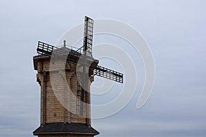 A windmill made of wooden beams against a cloudy autumn sky. A tall building made of wood