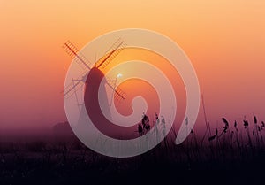 Windmill in the mist at sunrise. A yellow windmill rises from a misty field