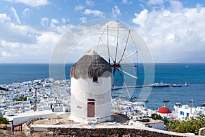 Windmill on mountain by sea in Mykonos, Greece. Windmill on seascape on cloudy sky. White building with sail and straw