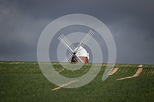 A windmill poking over a hill surrounded by newly planted crops