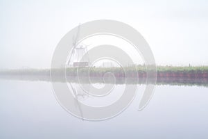 Windmill reflected in river and dense fog