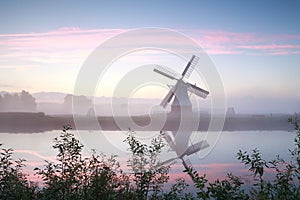 Windmill by river at misty sunrise