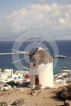 Windmill by sea in Mykonos, Greece. Windmill on mountain landscape cloudy sky. Whitewashed building with sail and straw