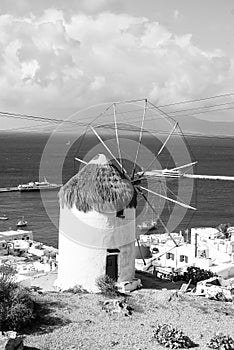 Windmill by sea in Mykonos, Greece. Windmill on mountain landscape cloudy sky. Whitewashed building with sail and straw