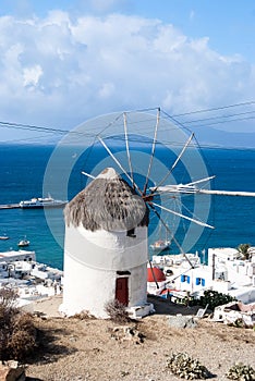 Windmill by sea in Mykonos, Greece. Windmill on mountain landscape cloudy sky. Whitewashed building with sail and straw