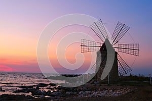 Windmill on the shore seaside with sunset in the background. North of Sicily, Trapani, old fashioned windmill on the