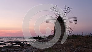 Windmill on the shore seaside with sunset in the background. North of Sicily, Trapani, old fashioned windmill on the