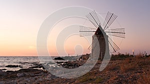 Windmill on the shore seaside with sunset in the background. North of Sicily, Trapani, old fashioned windmill on the