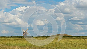 Windmill standing lonely on field with forest and cloudscape on background. Rural green landscape with mills and cloudy