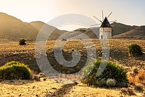 Windmill at sunset between the hills. Light and golden fields in southern Spain.