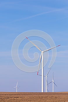 Windmill turbines on agricultural field with blue sky in background. Renewable energy wind turbine