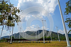 Windmill white post and solar cell panel technology to generate clean renewable energy on grass yard with green mountain, blue sky