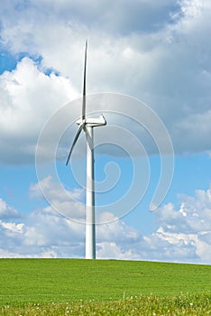 Windmill. A windmill on a green hill against cloudy blue sky with copy space. Wind turbines generate electricity through