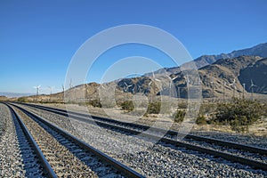 Windmills along a railroad track with mountains and clear blue sky views