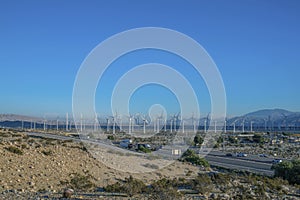 Windmills along road with cars against mountain and blue sky background