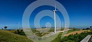 Windmills farm or Wind turbine power generators standing on green mountain against a blue sky at Phetchabun Province, Thailand.