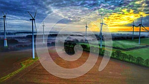 Windmills generating Wind energy on grass lawns under sunrise cloudy sky