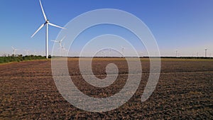 Windmills in a plowed field. Wind farm with turbine cables for wind energy. Renewable energy source, earth care. Drone video of