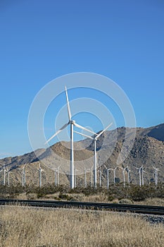 Windmills and railroad track with clear blue sky and mountains on a sunny day