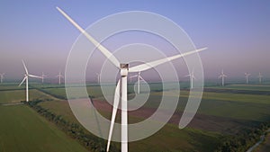 Windmills with rotating wings among green fields. Wind farm with turbine cables for wind energy. Renewable energy source, earth