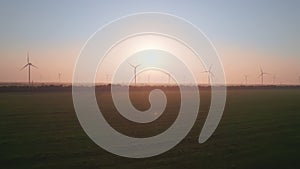 Windmills with rotating wings at sunset or sunrise. Technology for wind energy, renewable energy source, earth care. Wind power