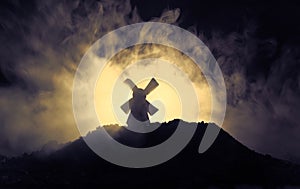 Windmills is silhouette against the night sky. Night decor with old windmill on hill with horror toned foggy background with light