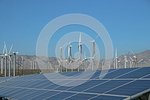 Windmills and solar panels against mountain and blue sky background