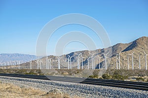Windmills or windpumps along railroad track on a wind park with blue sky
