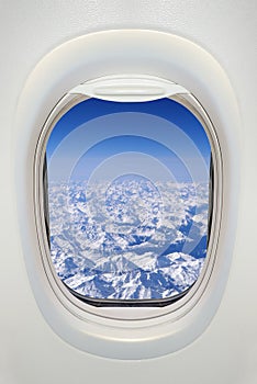 Window of an airplane from inside, view on snowy mountains