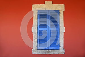 Window with blue shutters in old red stucco house