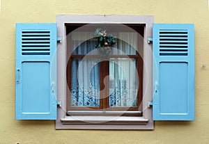 Window with blue wooden shutters on a beige wall and Christmas decoration