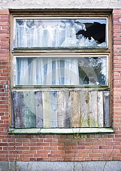 Window boarded up by wooden panels in an old red brick house