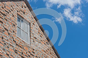 Window on brown brick wall and wooden roof in vintage style with blue sky background.