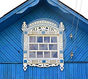 Window with carved platbands under a roof of the blue house