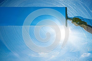 Window cleaner cleaning window with squeegee and wiper on a sunny day with a bright blue sky photo