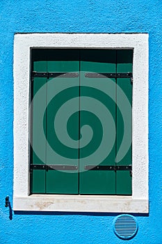 Window with closed green shutter on blue wall. Italy, Venice, Burano