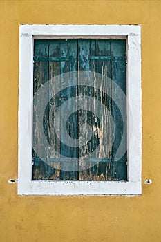 Window with closed old green shutter on yellow wall. Italy, Venice, Burano