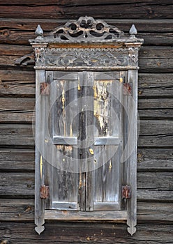 Window with closed shutters and decorative wooden elements on the wall of a wooden house