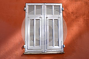Window closed with white wooden shutters. on a red wall