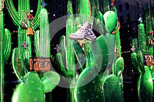 Interesting window display of upscale purses and sneakers set on bright green cactus plants, 5th Avenue, New York City, 2018