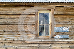 A window in the exterior wall of a vintage wood building with a corrugated metal roof