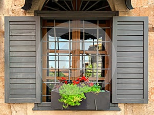 A window with flower pot, metal grill and  wooden shutters of an historical stone house in old town of Antalya Kaleici, Turkey.